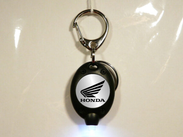 LLAVERO DE PLASTICO Y METAL CON UNA LUZ LED QUE HACE DE LINTERNA. VISTA FRONTAL ENCENDIDO.