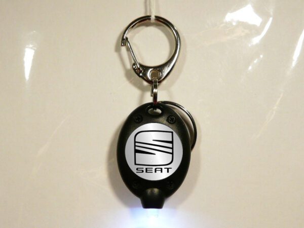 LLAVERO DE PLASTICO Y METAL CON UNA LUZ LED QUE HACE DE LINTERNA. VISTA FRONTAL ENCENDIDO.
